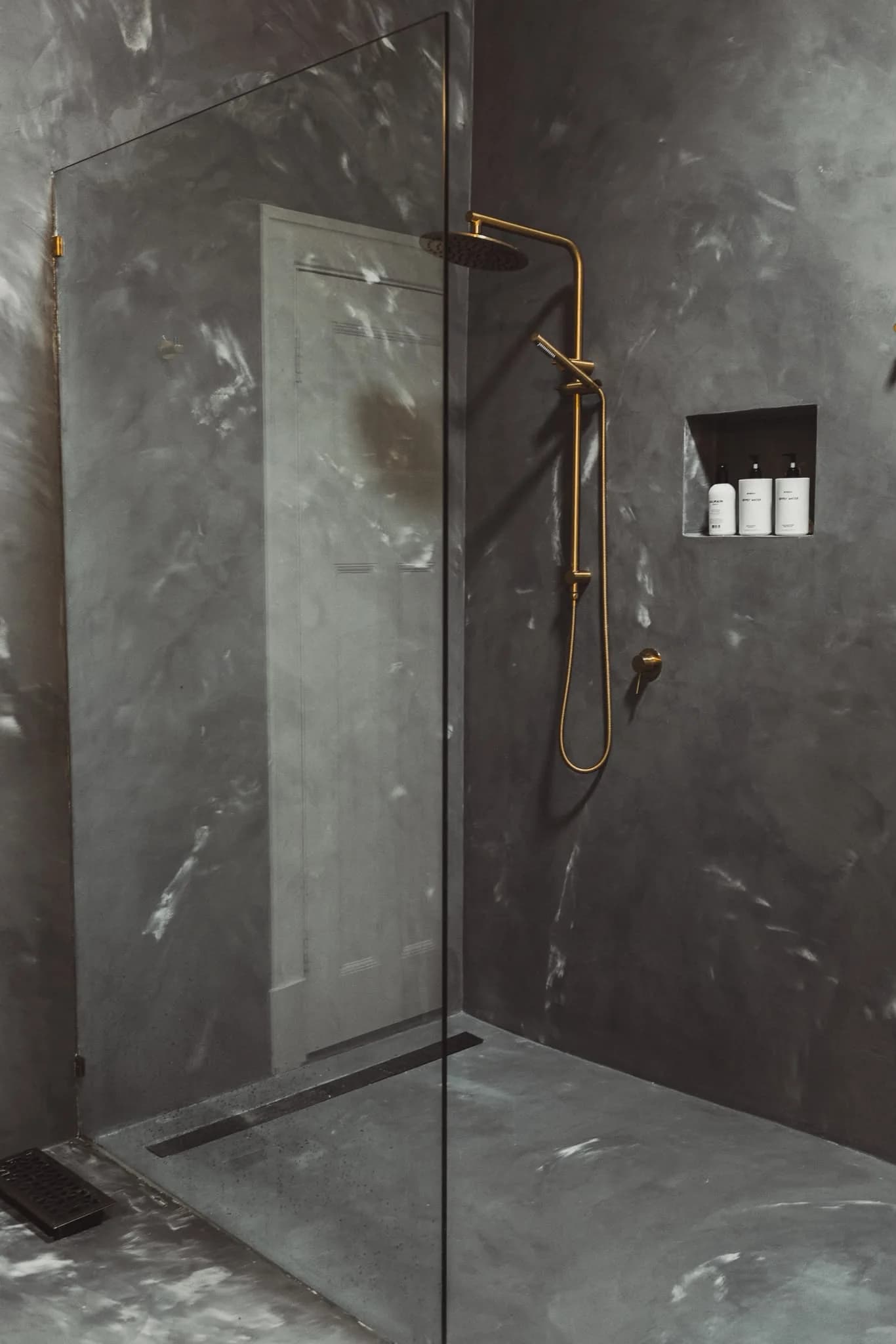 Shower in dark grey marbled microcement with a brass rail shower and a wall niche