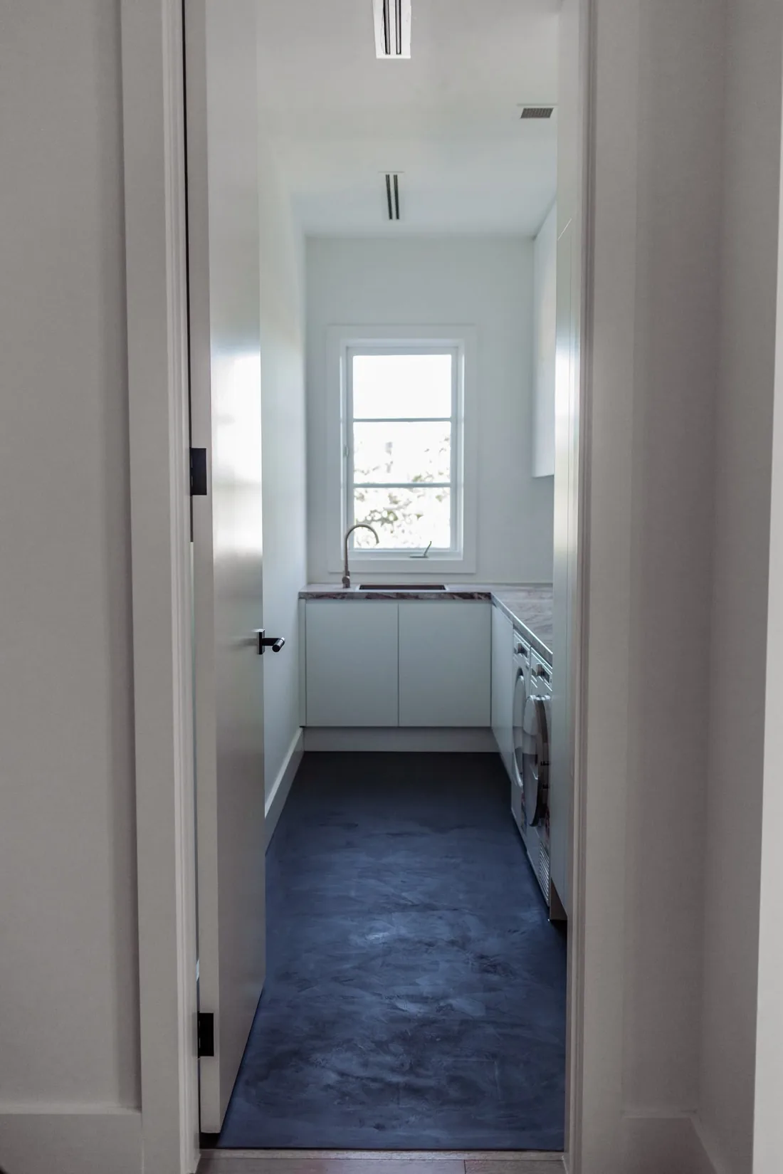 Dark microcement floor in a white laundry, seen through the doorway