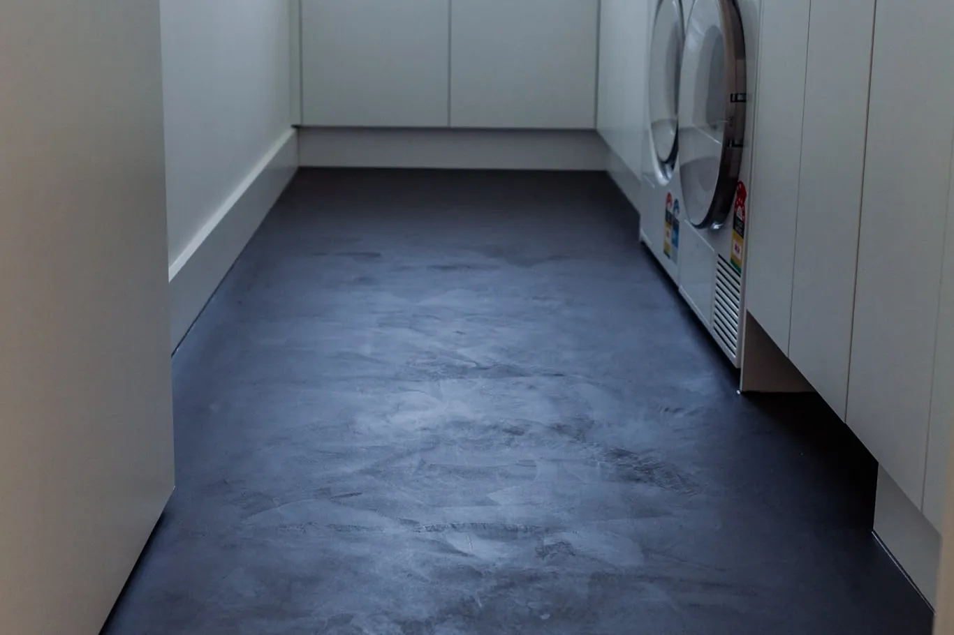 Laundry with a dark microcement floor, white cupboards and a washer and dryer