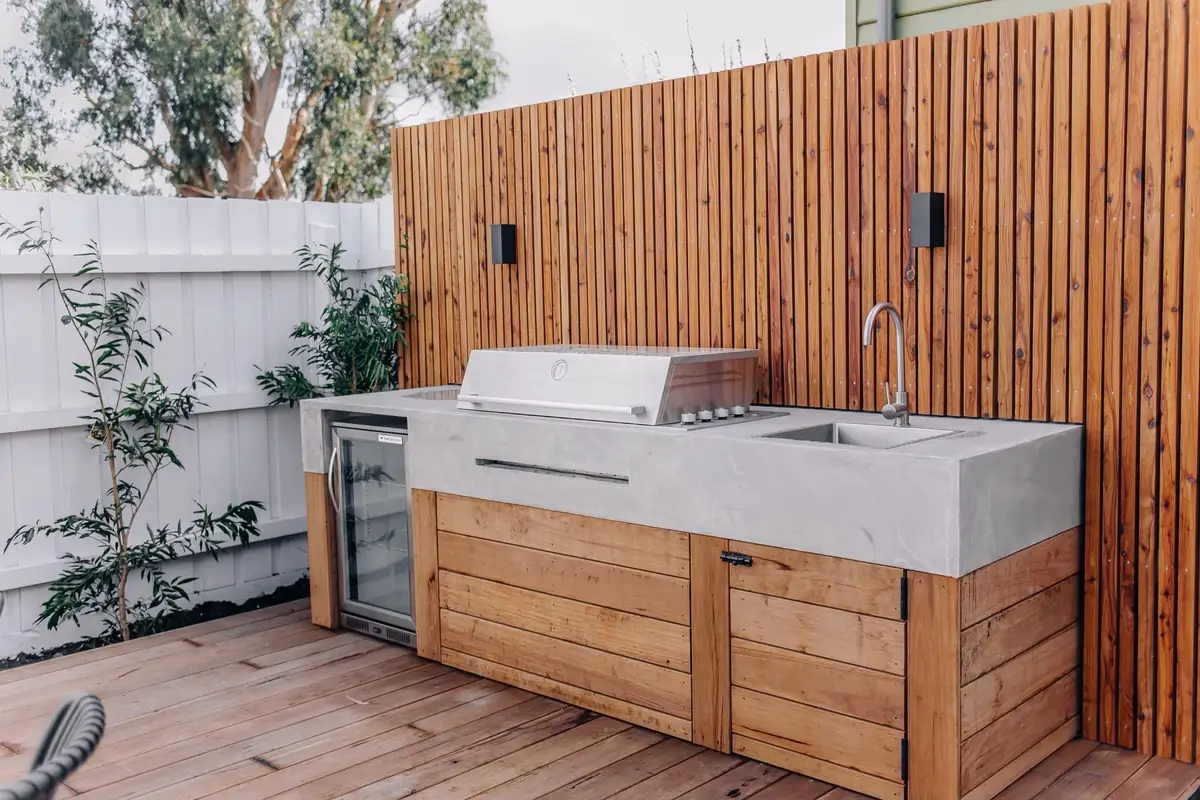 Outdoor kitchen with a grey microcement benchtop over timber cupboards, a barbecue and a sink