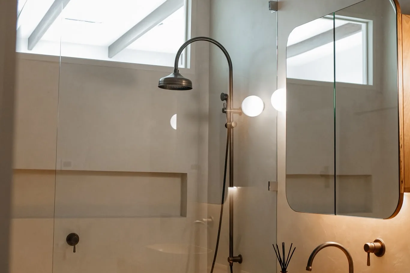 Microcement shower in soft beige with a bronze rail shower, a long niche and a timber-framed mirror cabinet